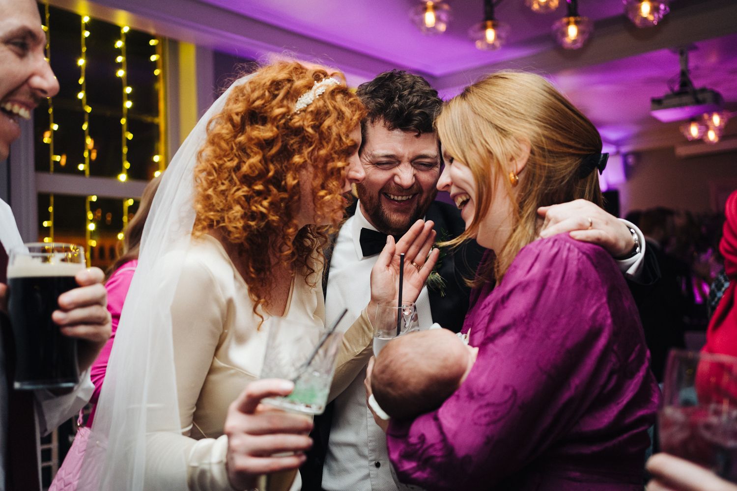 Joyful candid moment between wedding guests at a reception with purple mood lighting.