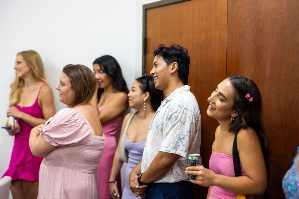 Wedding guests in pink dresses stand together during celebration indoors.