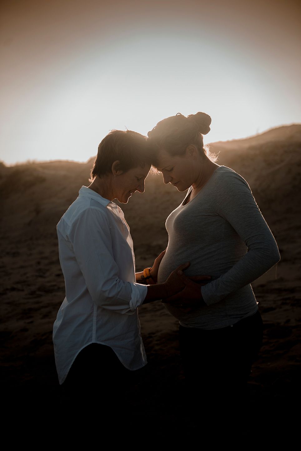 Couple embracing during a Maternity session at golden hour with warm sunset light in the background.