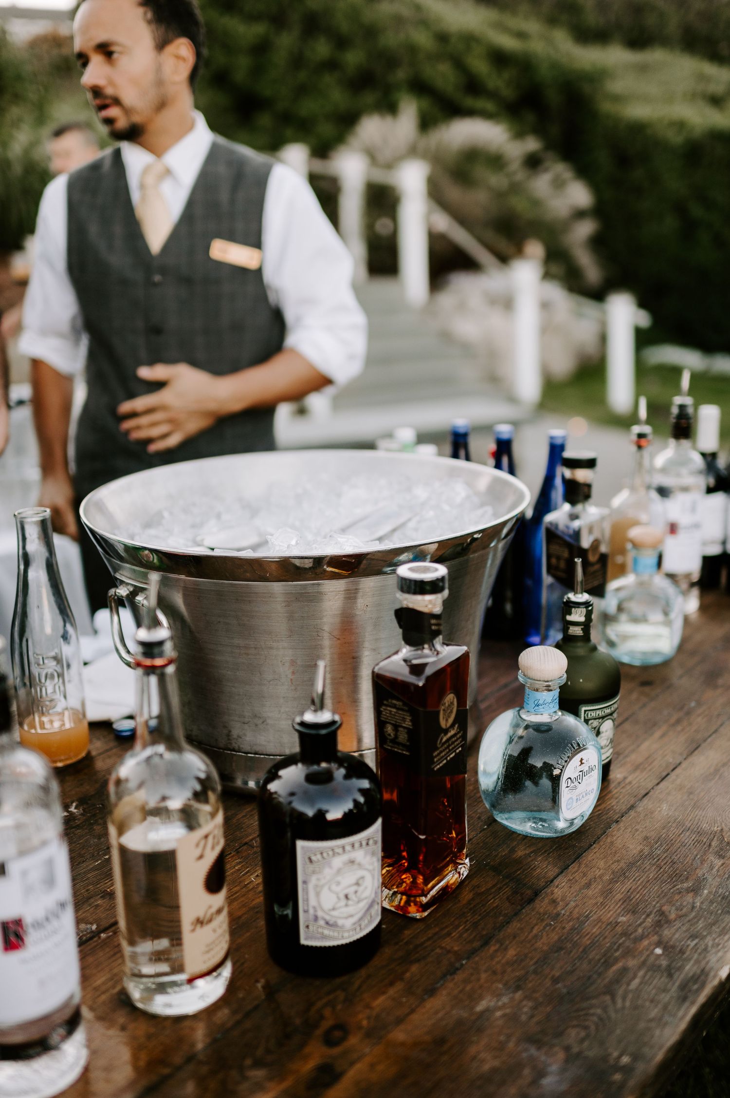 Collection of premium liquor bottles arranged on wooden bar at wedding event.