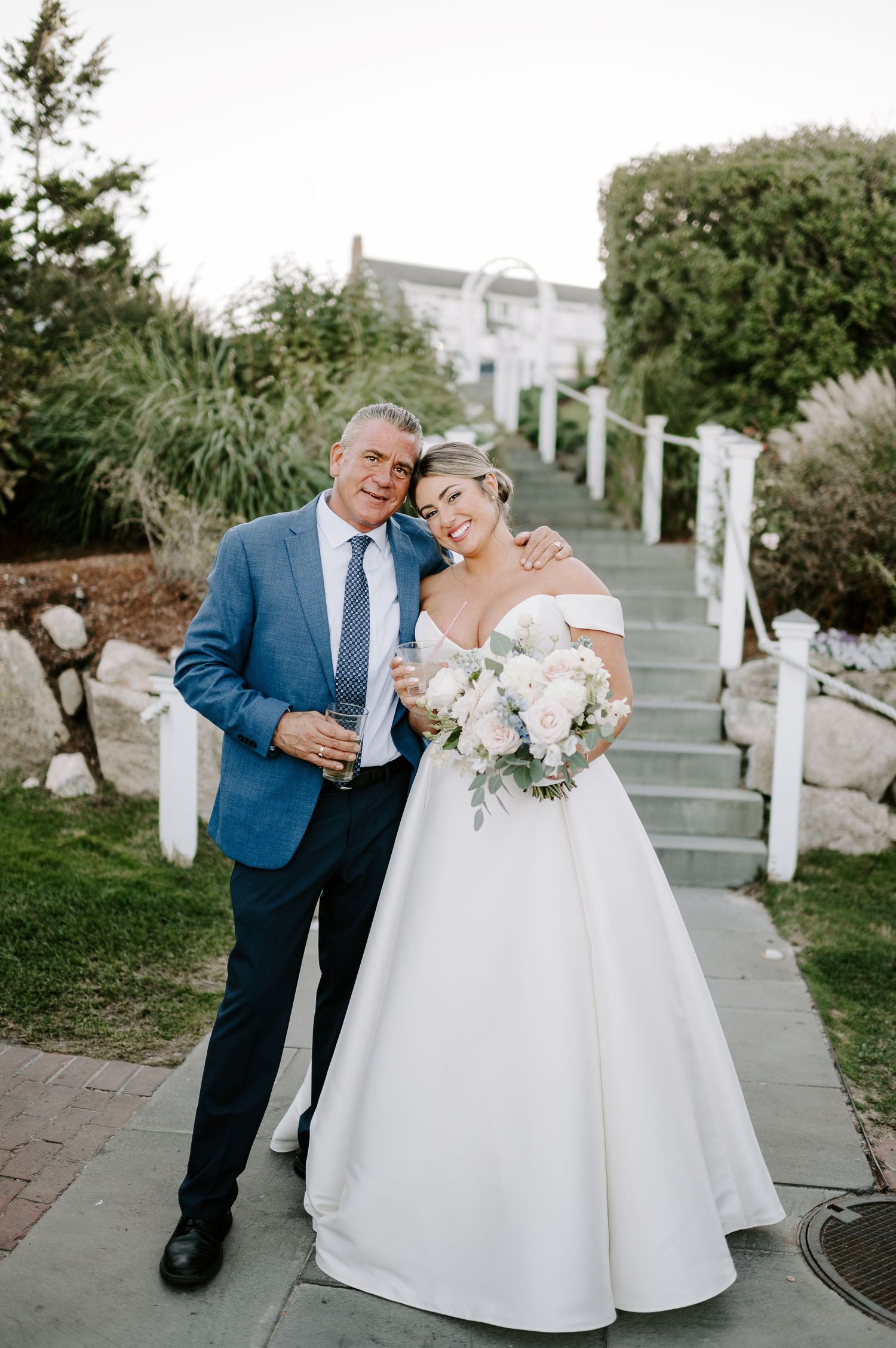 Elegant wedding couple poses on stone pathway surrounded by lush greenery.
