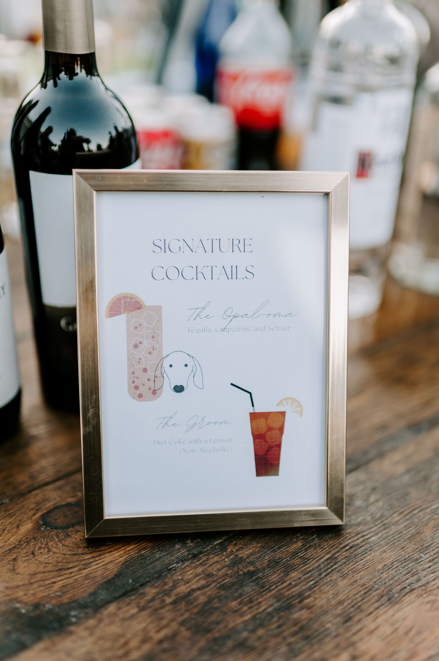 Signature cocktail menu cards displayed on rustic wooden table at wedding reception.