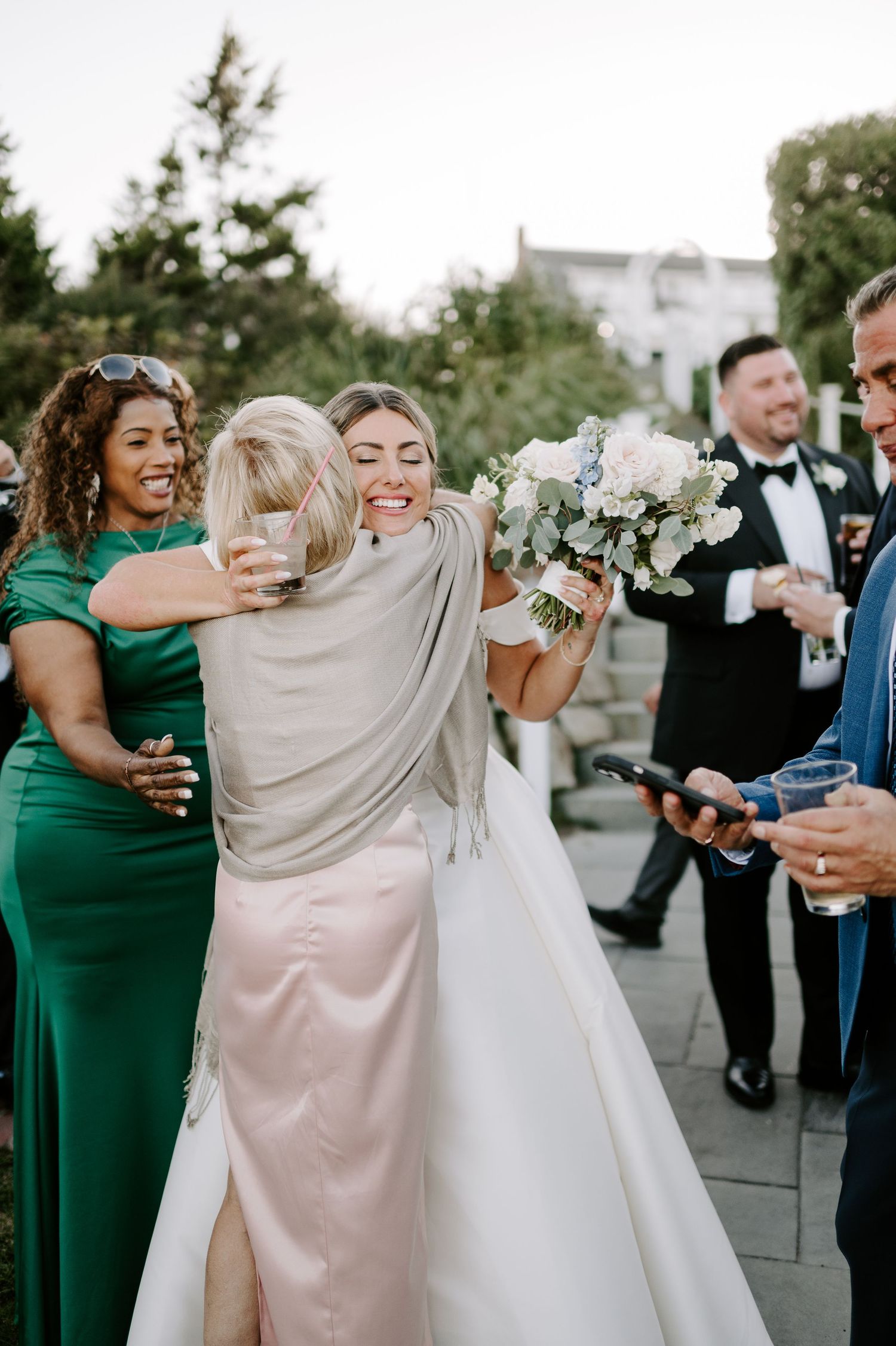 Wedding party celebrates outdoors with bridesmaids wearing emerald green and blush dresses.