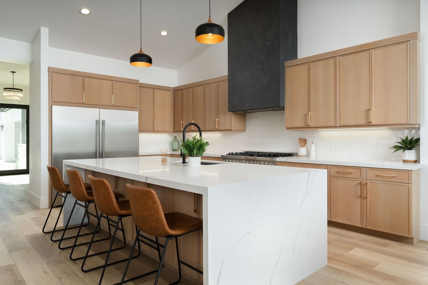 Contemporary kitchen with light wood cabinets, white island and brown leather barstools under pendant lighting.