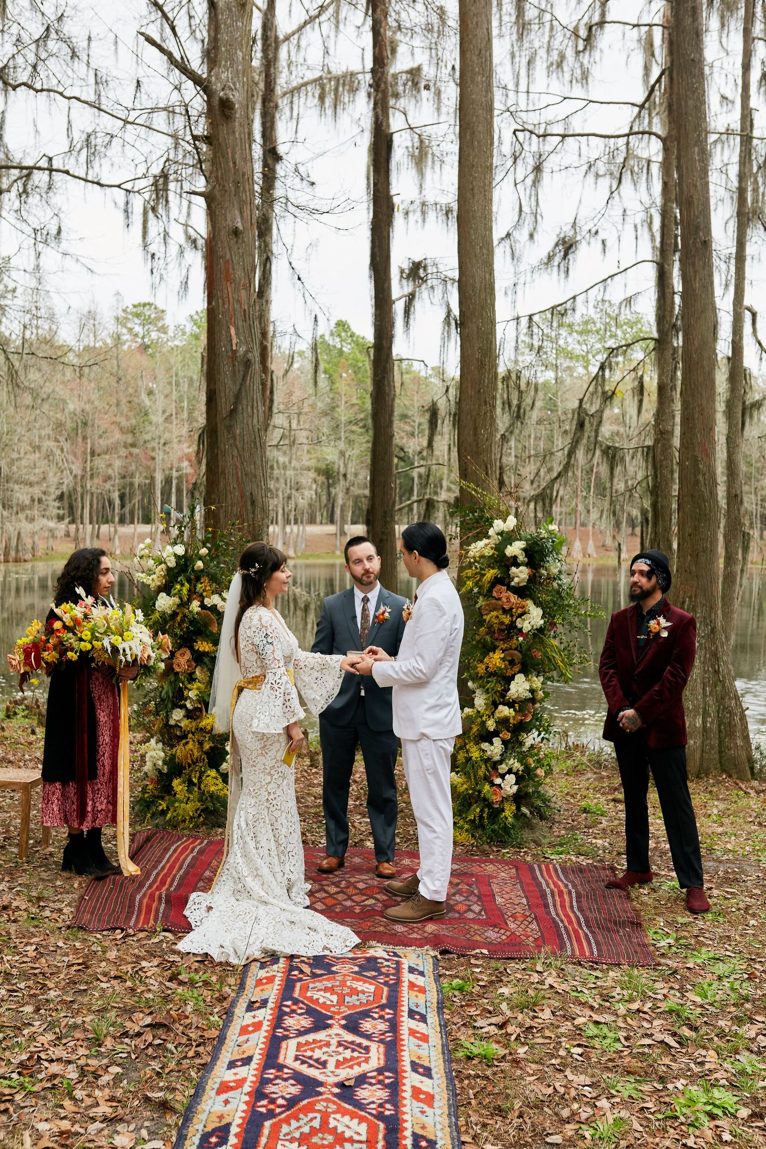 Outdoor forest wedding ceremony with floral arch and Persian rugs on autumn ground.