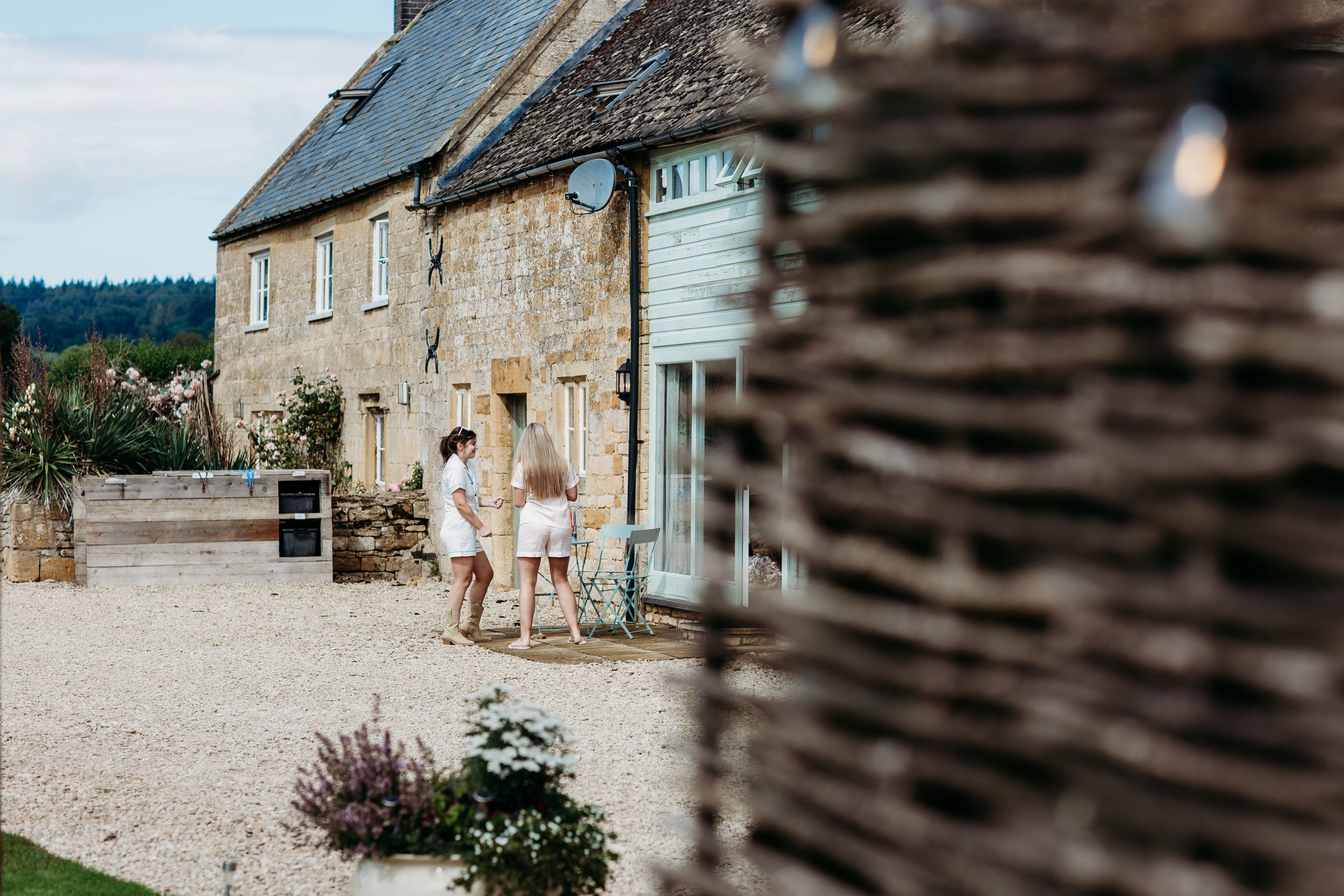 White-clothed figures walk near a stone cottage on a gravel path.
