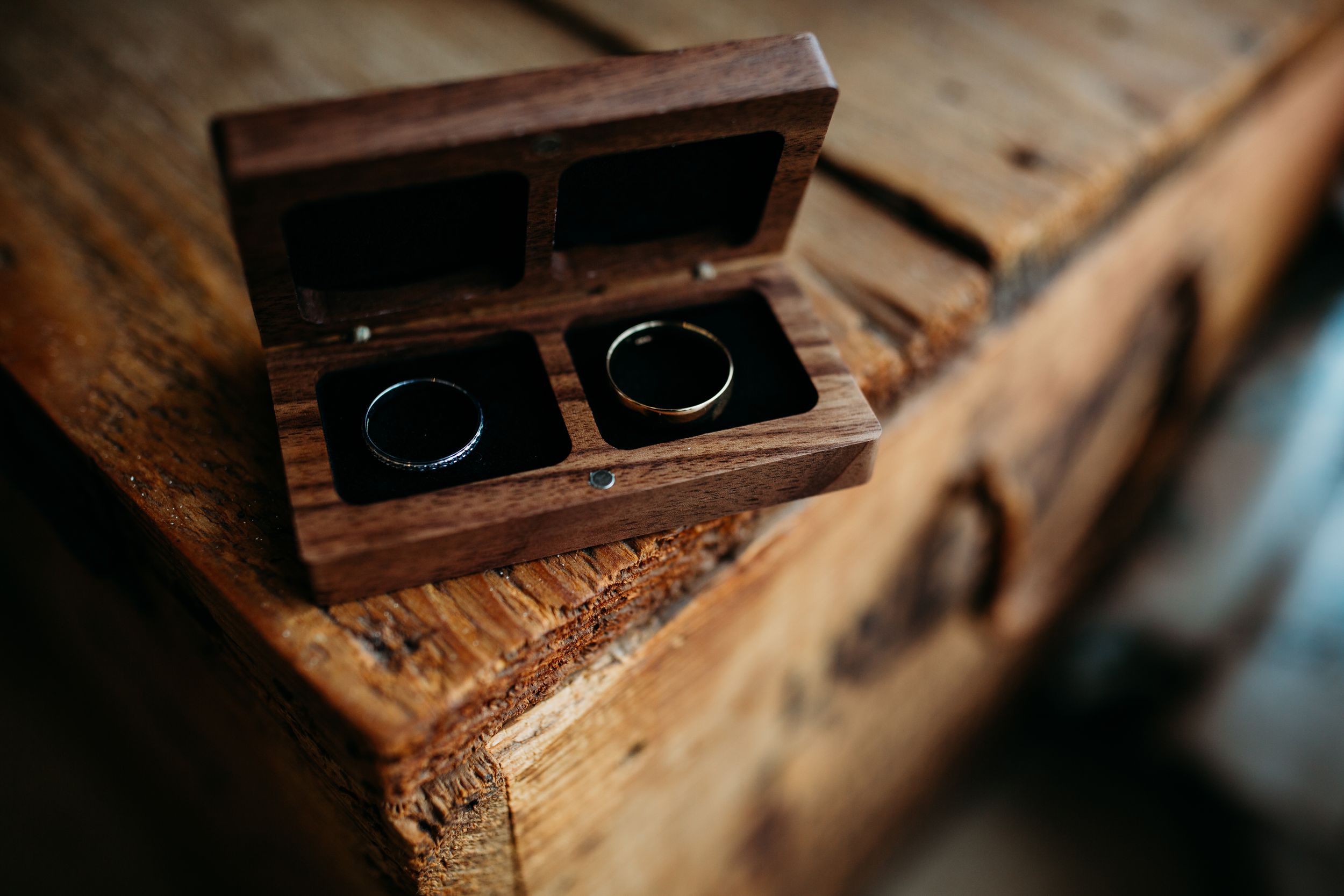 Wedding rings nestled in vintage wooden box on rustic wooden surface.