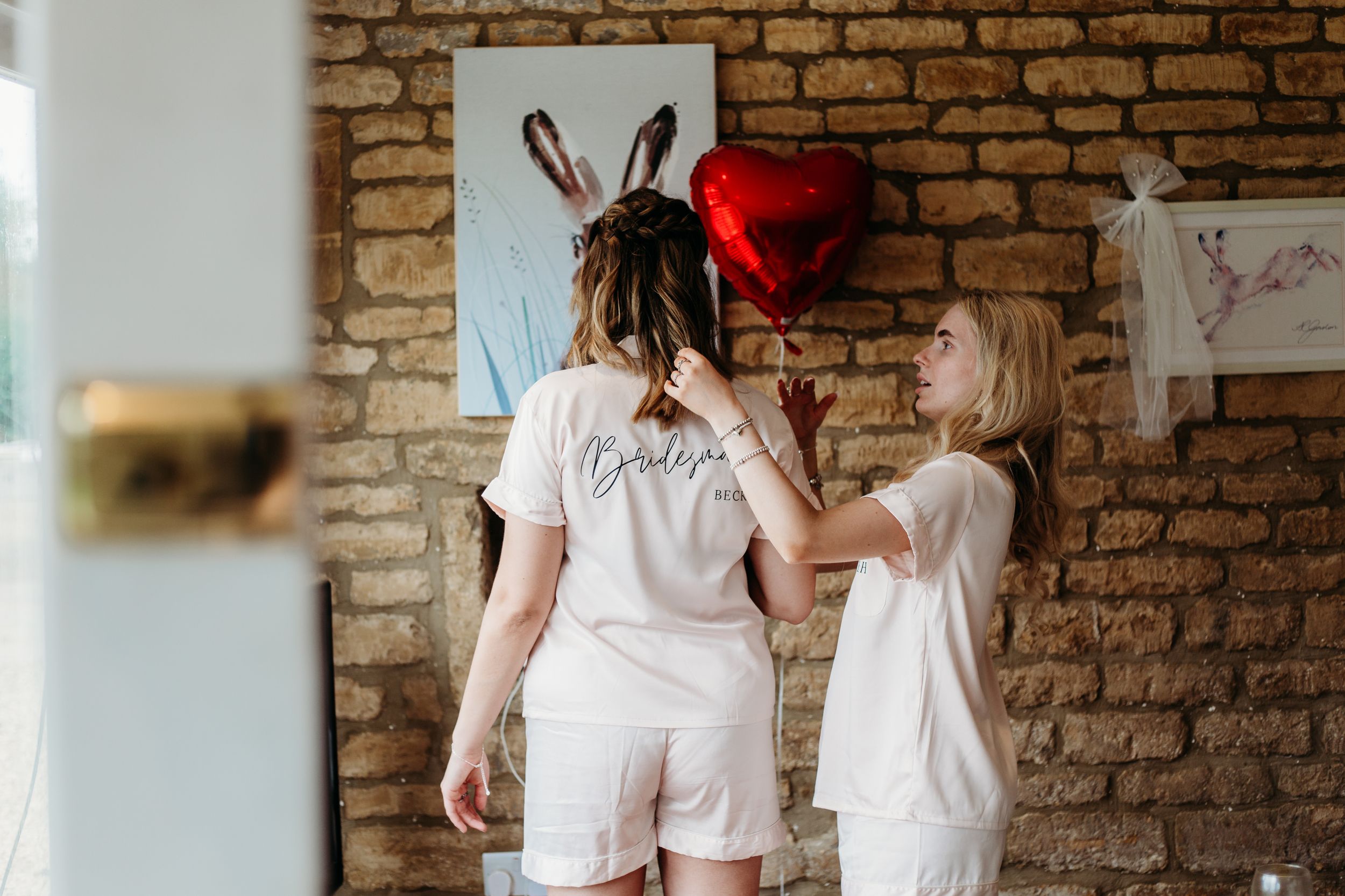 Two people in white outfits drawing on brick wall with heart balloon decoration.