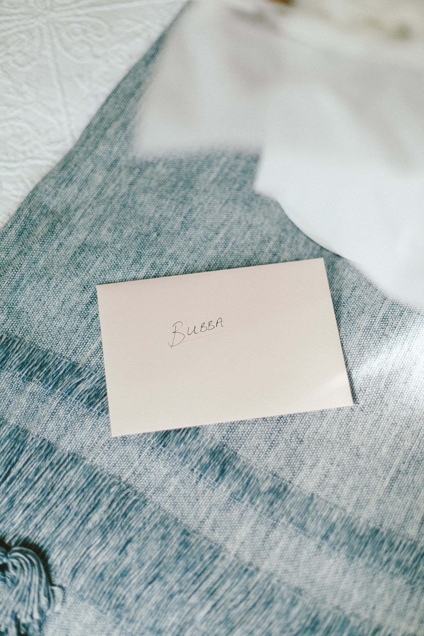 Simple white place card with handwritten text on blue-grey textured surface.