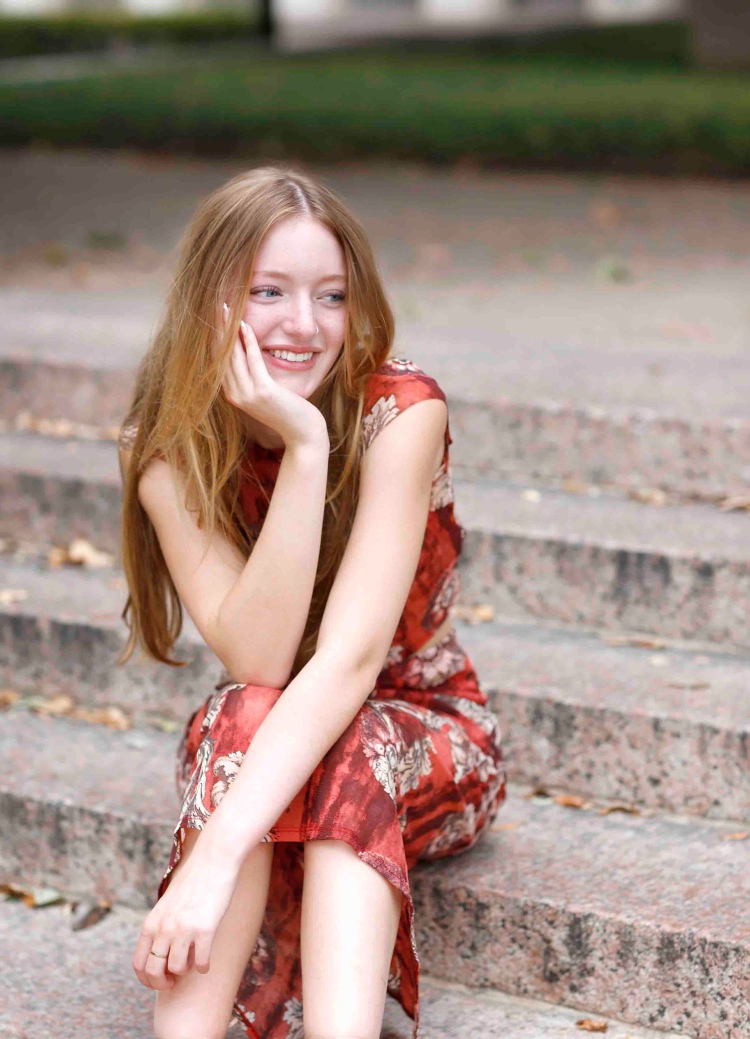 Casual outdoor portrait featuring a red floral dress and relaxed pose on concrete steps.