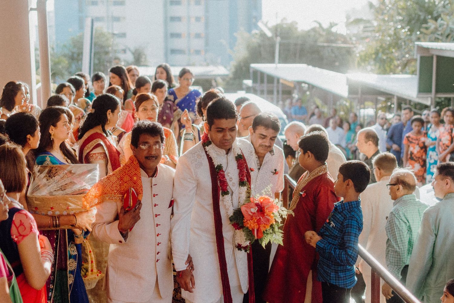 Outdoor wedding procession with attendees in colorful traditional Indian clothing.