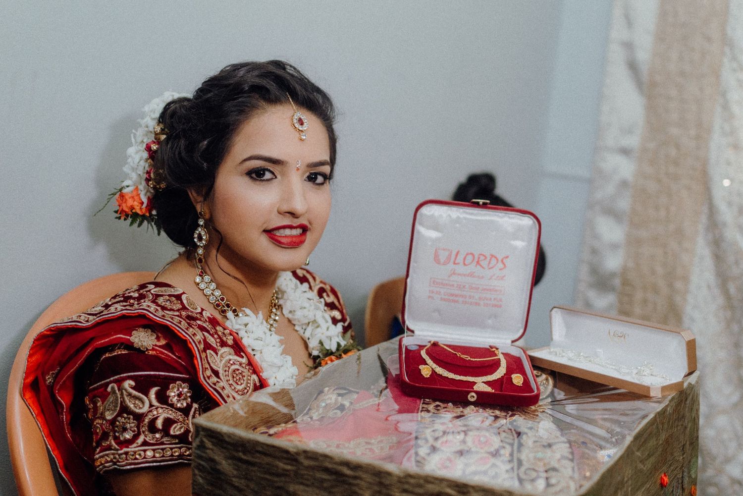 Traditional bridal attire with ornate red and gold sari shown next to a pink jewelry box on display.