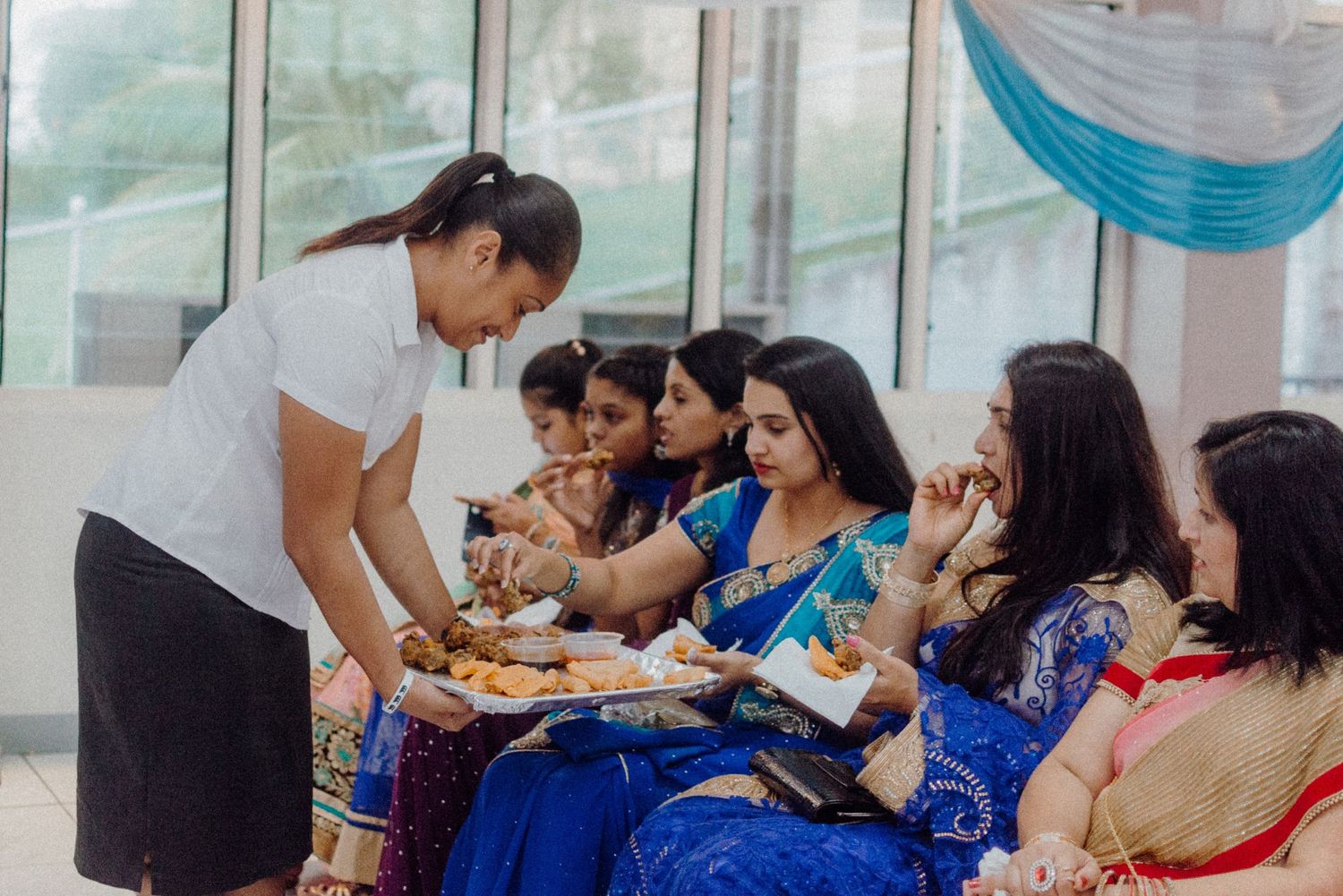 Server offering food to guests in colorful Indian formal wear at a celebration.