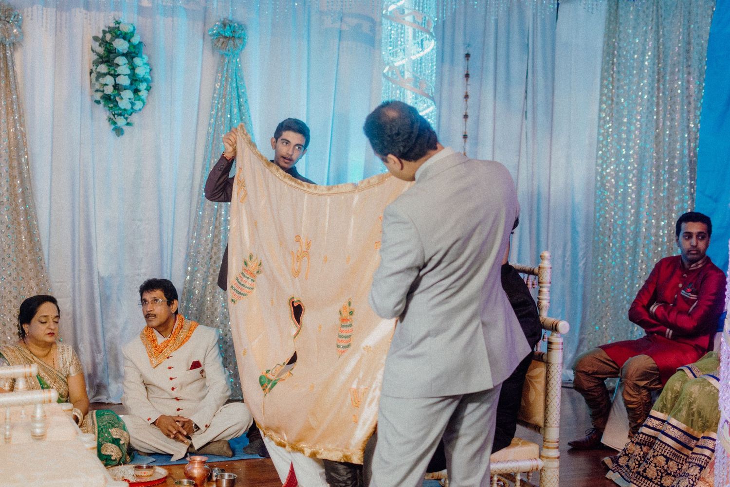 Traditional Indian ceremony with cloth being held up during ritual against blue backdrop.