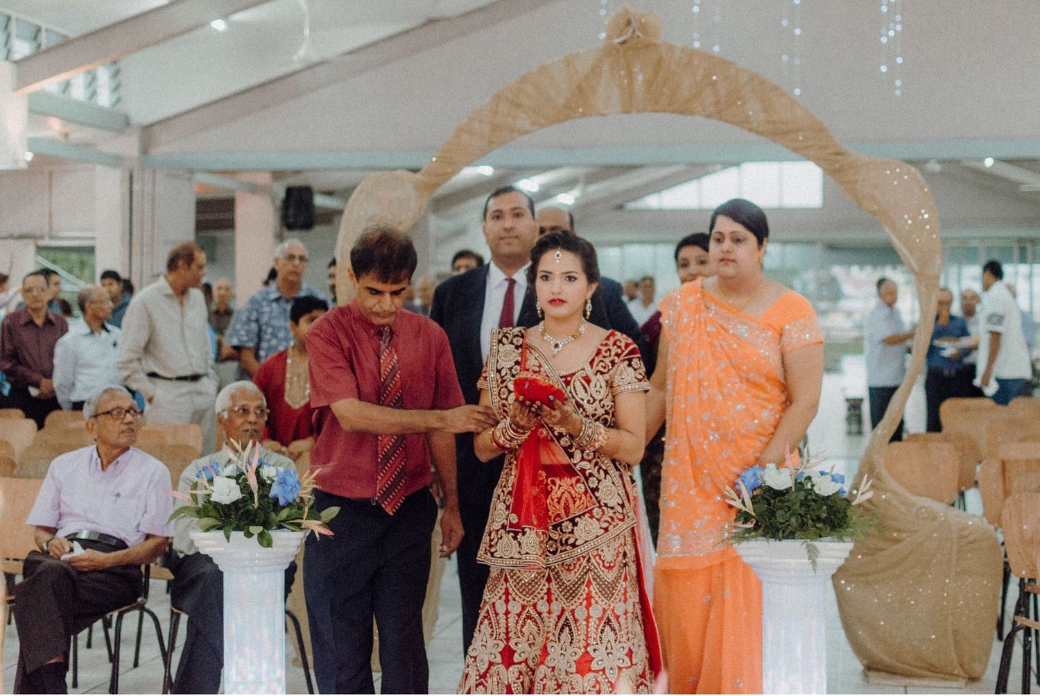 Wedding celebration with guests in traditional Indian attire under ornate arch.