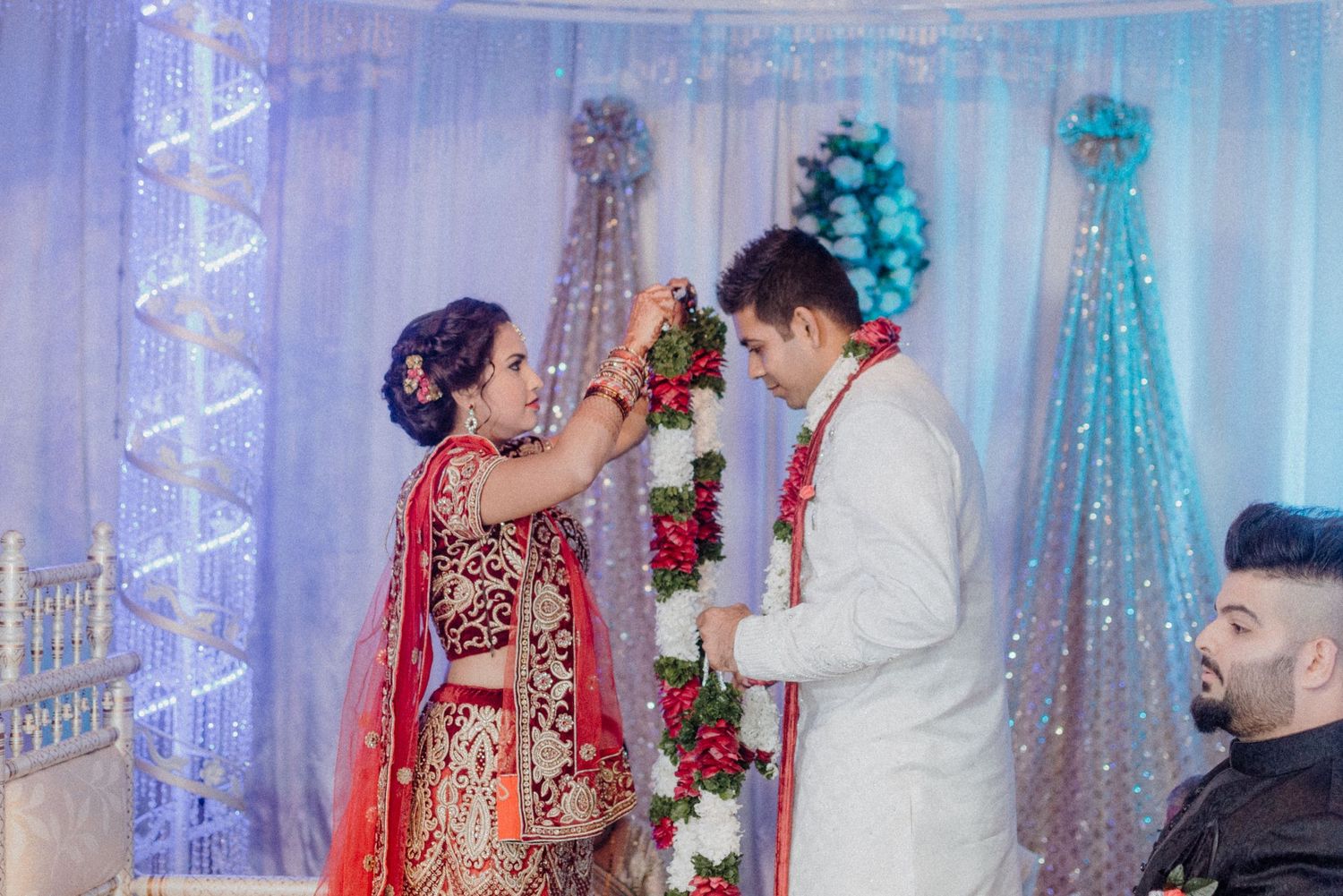 A traditional Indian wedding ceremony showing a couple participating in a garland exchange ritual under decorated decor.