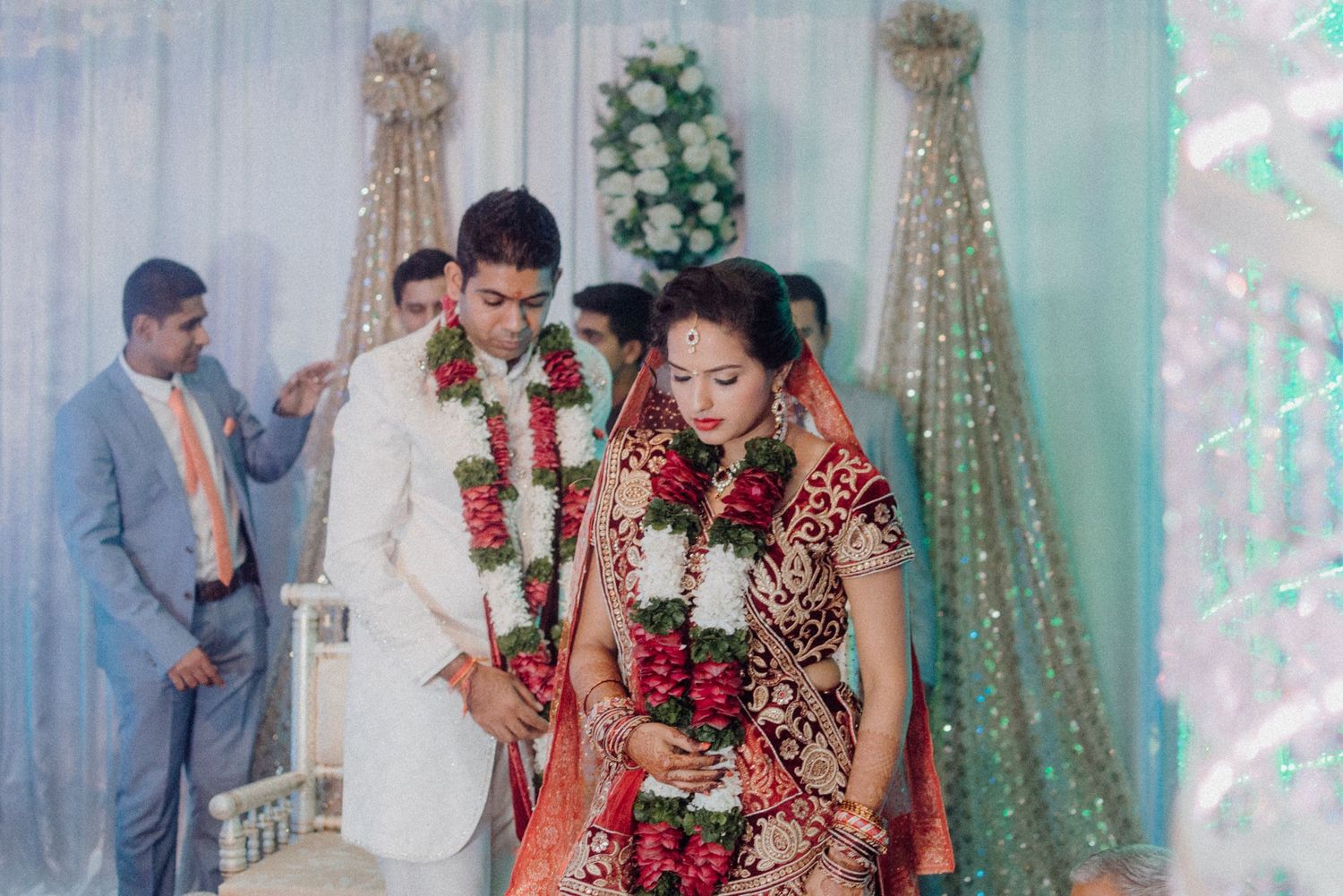 Couple in traditional Indian wedding attire during their ceremony under decorative lighting.