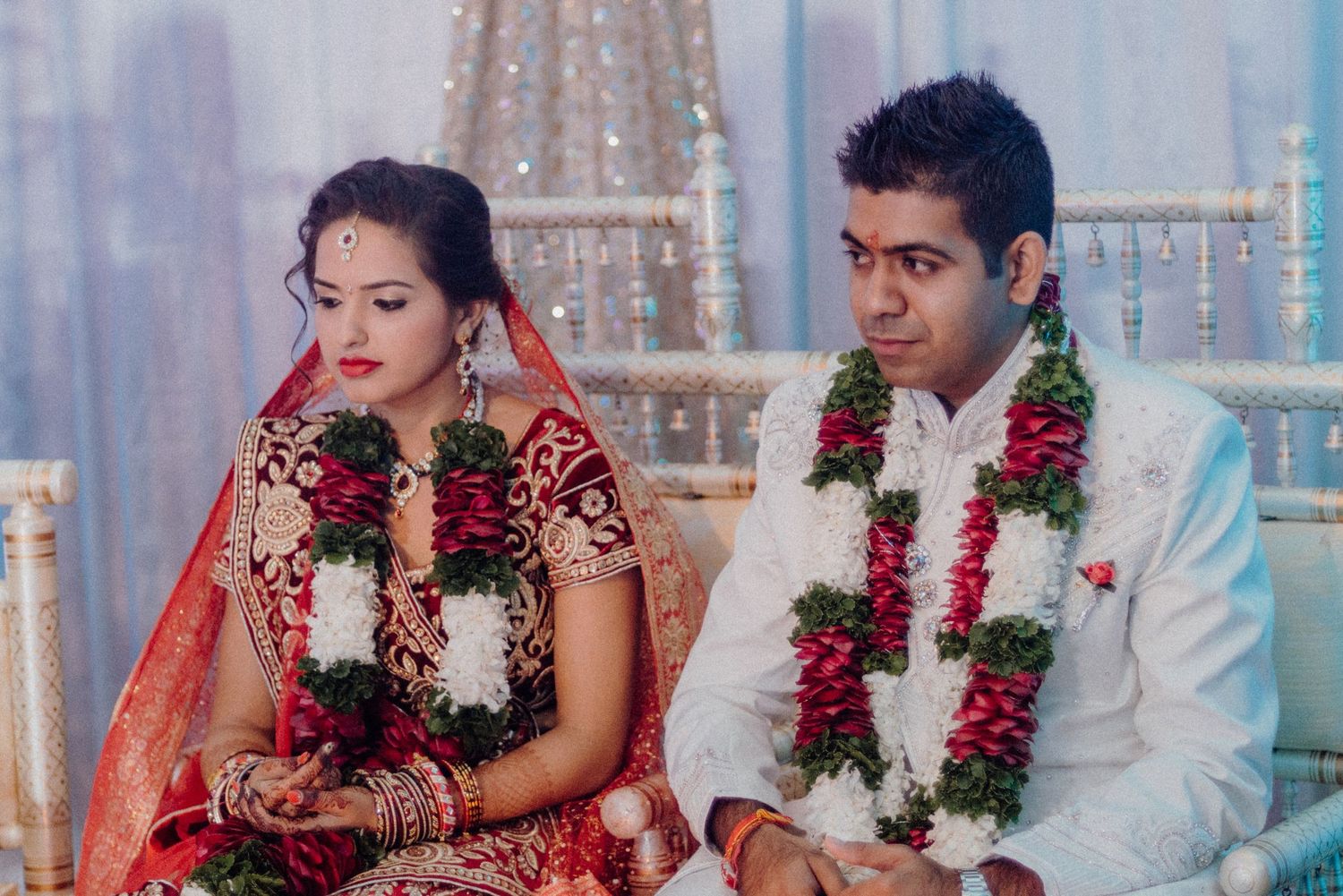 Newlyweds in traditional Indian wedding attire seated during ceremony wearing floral garlands.