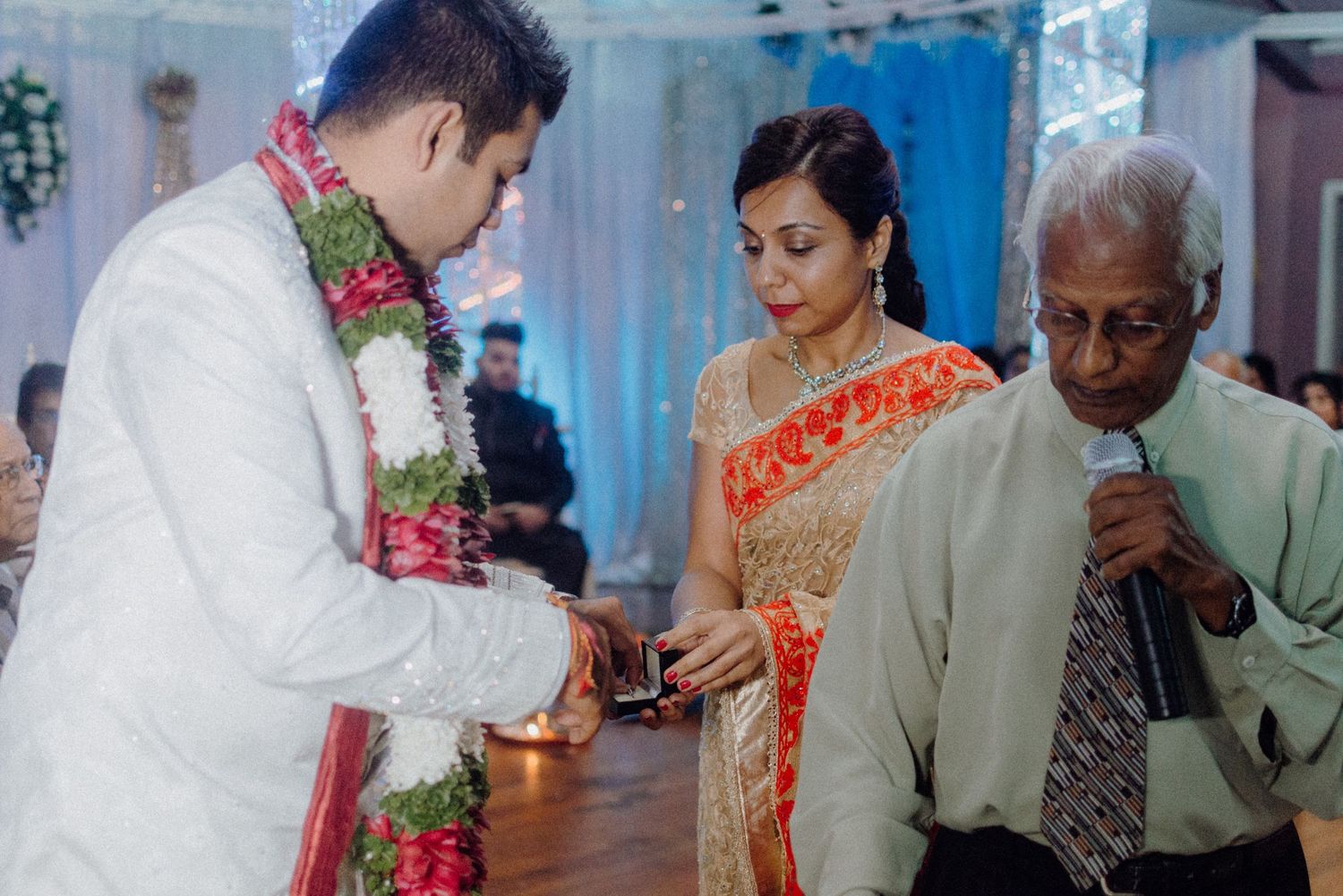 Traditional wedding ring exchange ceremony with participants in formal ethnic attire.