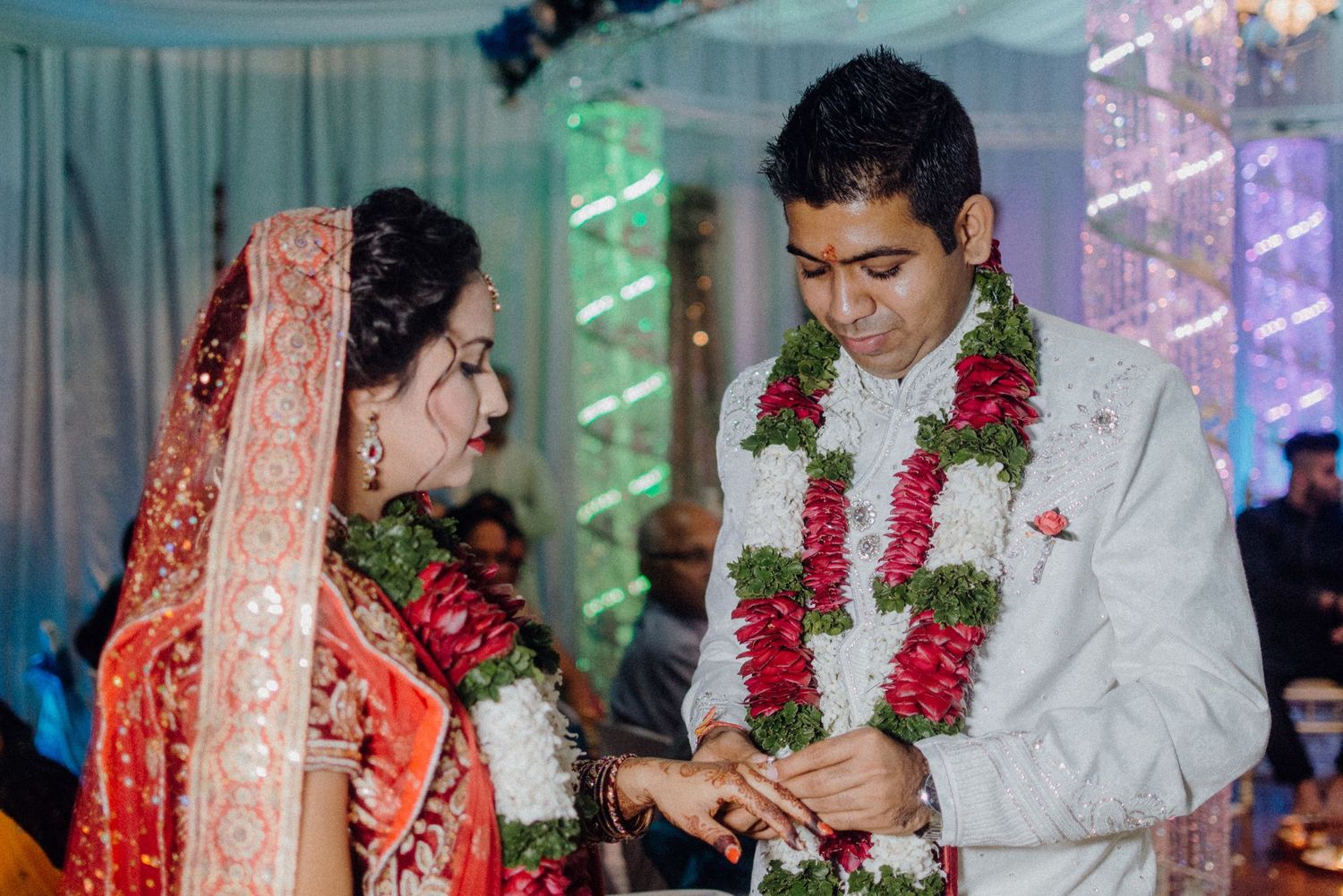 Wedding ceremony with couple in traditional attire exchanging rings against decorative backdrop.
