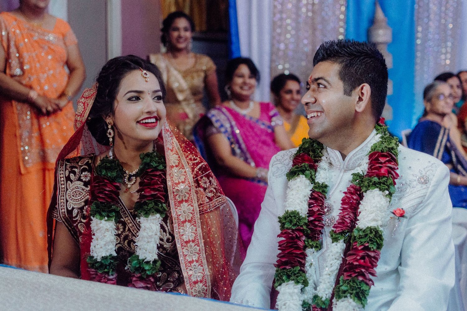 Wedding couple in traditional garlands and attire sharing a happy moment.