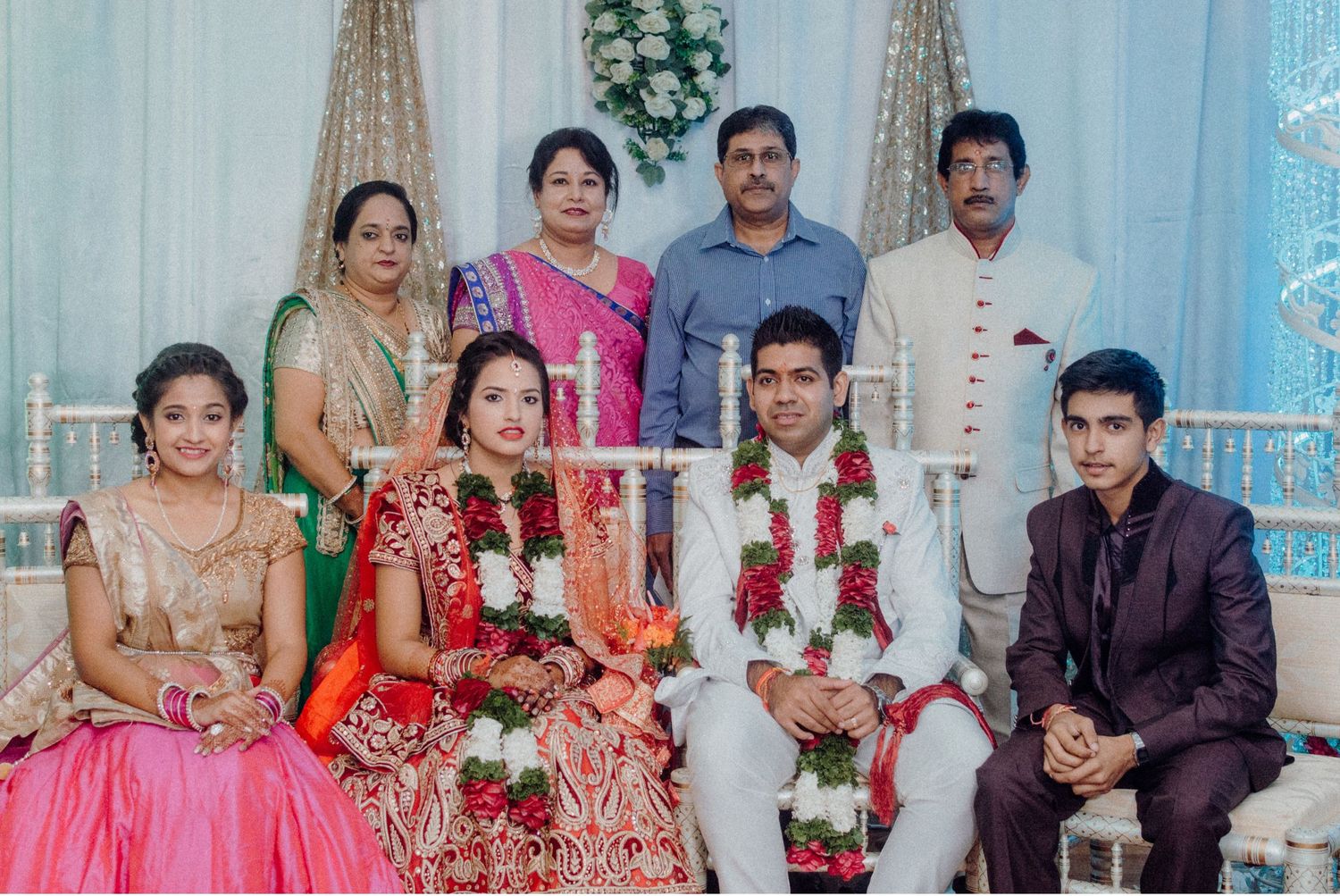 A traditional Indian wedding ceremony with family members gathered around the couple in elegant attire and floral decorations.