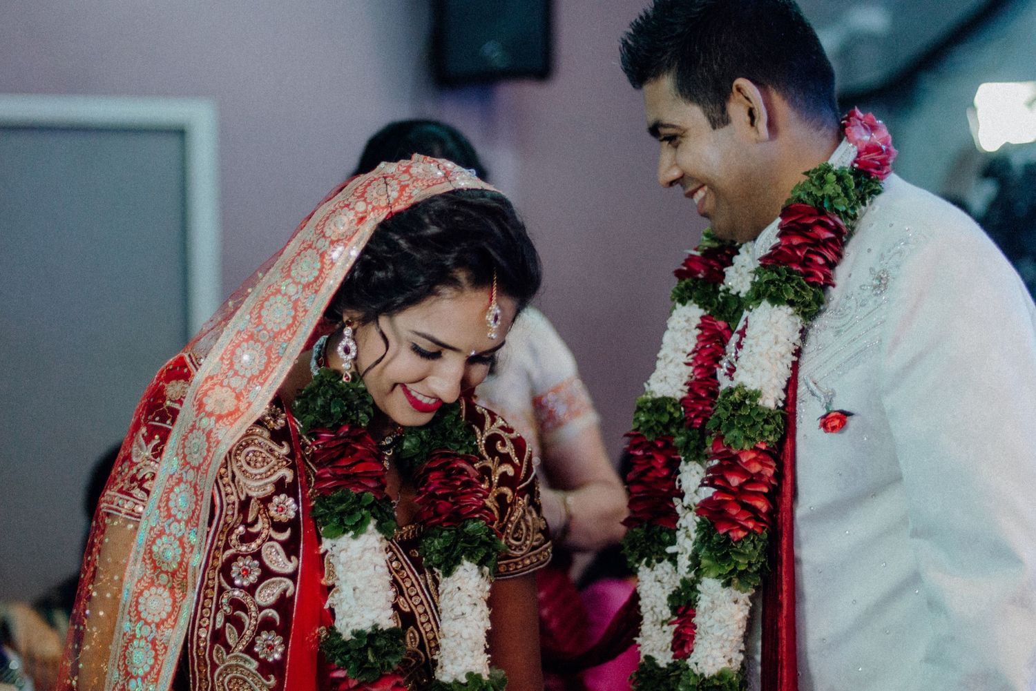 Candid moment of a couple sharing laughter during their wedding ceremony wearing floral garlands.