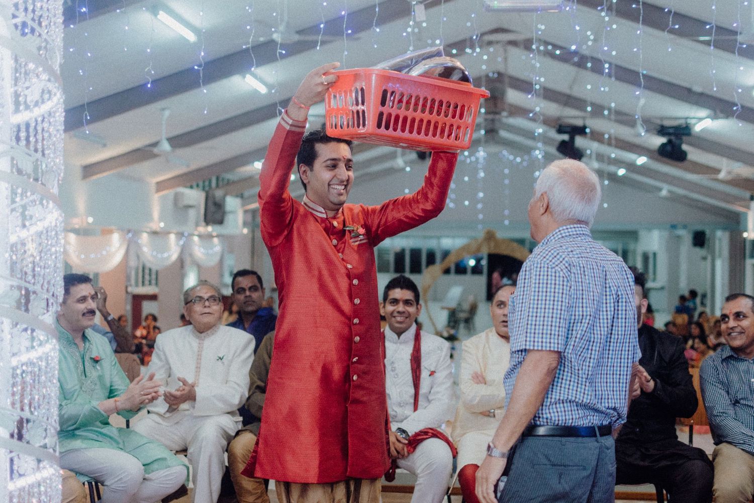 Guest in red kurta holding up a basket during a wedding celebration ceremony.