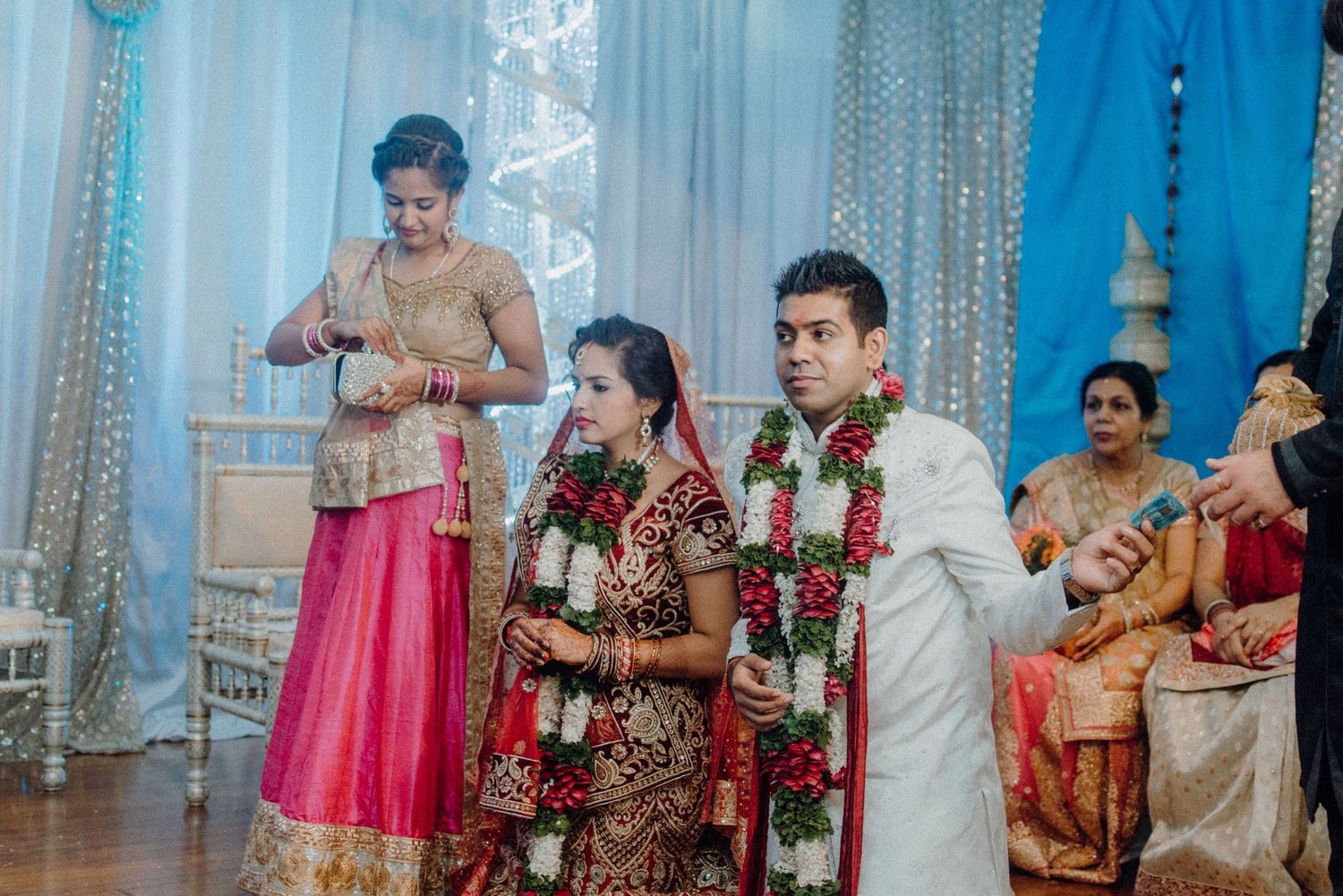 Wedding ceremony with couple in traditional Indian attire under decorative blue backdrop.