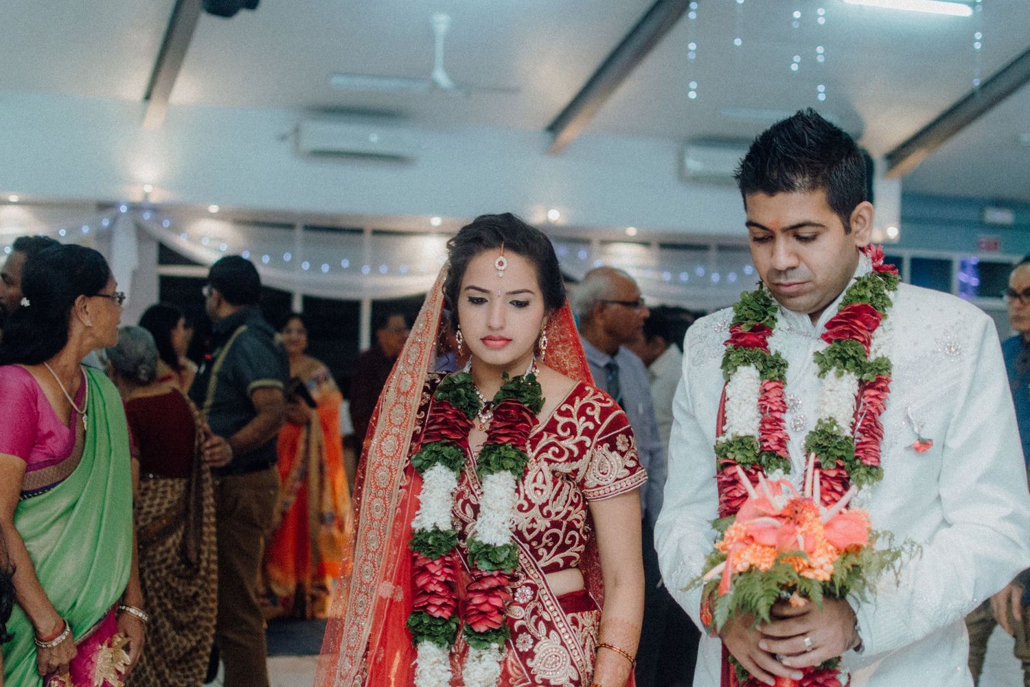 Couple in traditional Indian wedding attire walking with floral garlands.