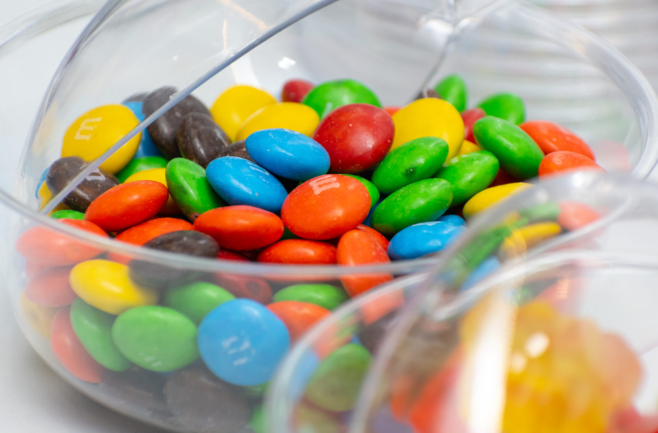 Colorful M&M candies in a clear glass bowl with vibrant yellow, red, green and blue pieces.