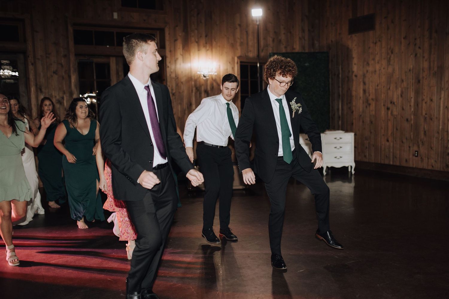 Groomsmen performing choreographed dance moves at a rustic wooden-paneled venue.