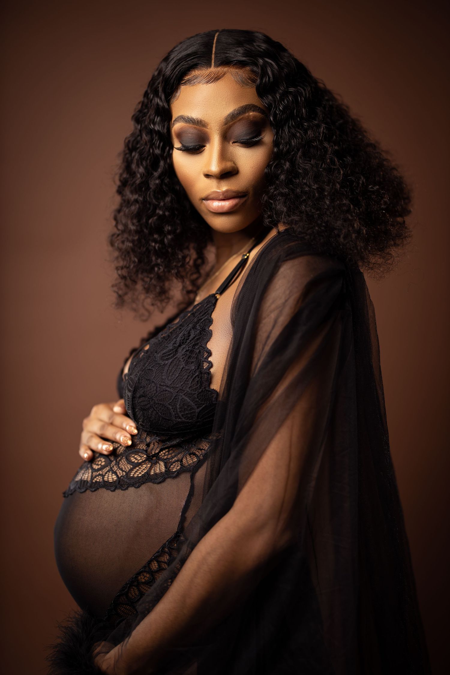 Intimate maternity portrait featuring woman in black lace against warm brown backdrop.