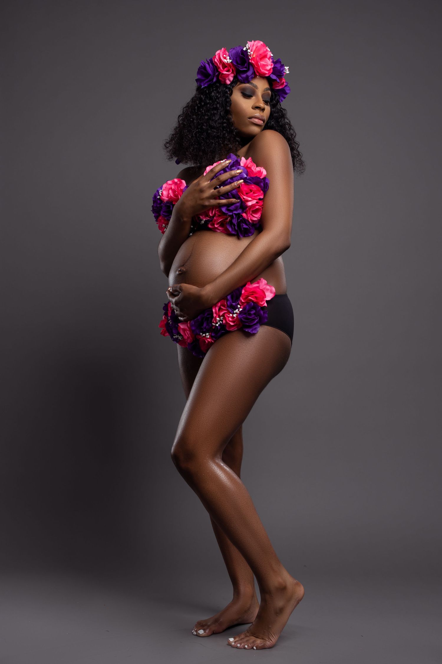 Artistic maternity pose with vibrant pink and purple floral accessories.