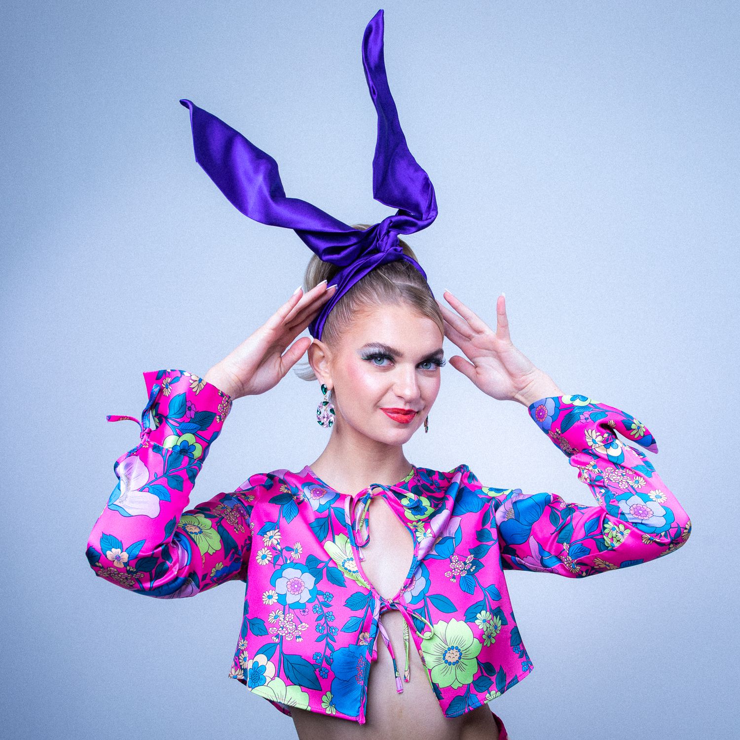 Colorful fashion photo with purple bow and floral print jacket against blue background.
