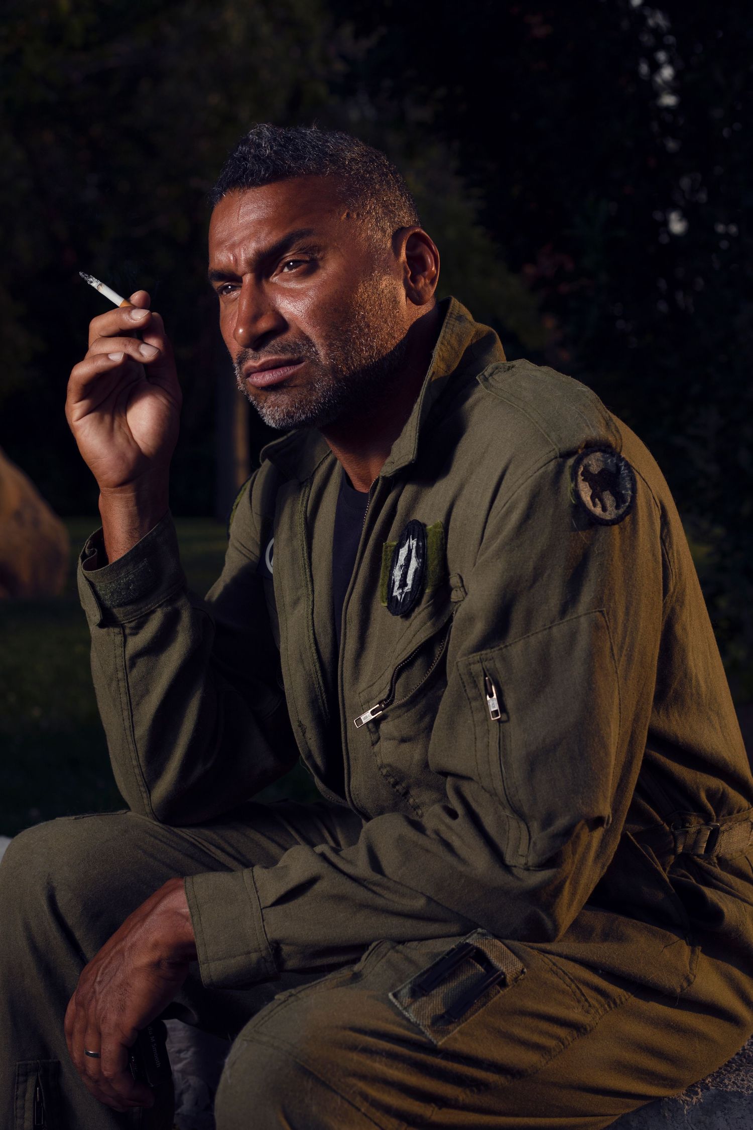 Moody portrait of person in military jacket smoking a cigarette at night.