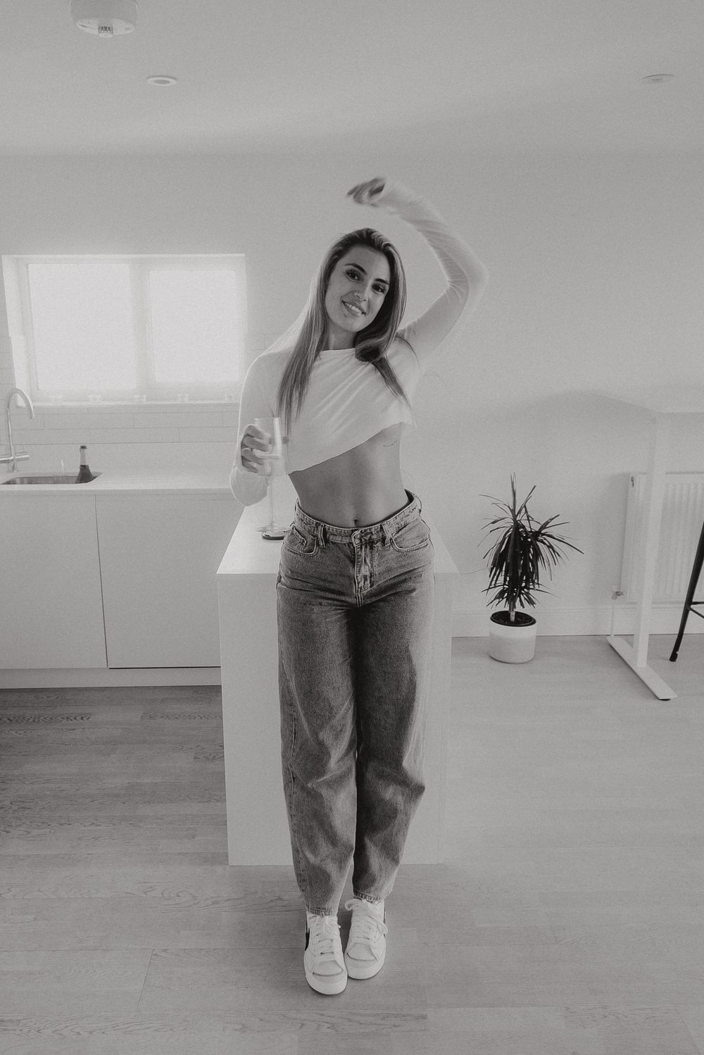 Casual indoor lifestyle portrait of person in jeans and crop top dancing in bright room.