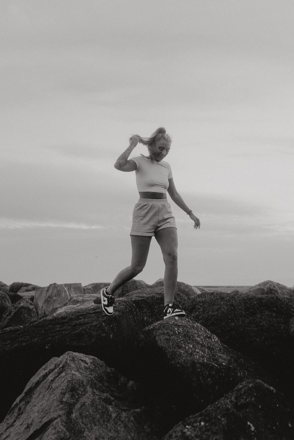 Silhouette standing on rocky outcrop against cloudy sky in black and white photograph.