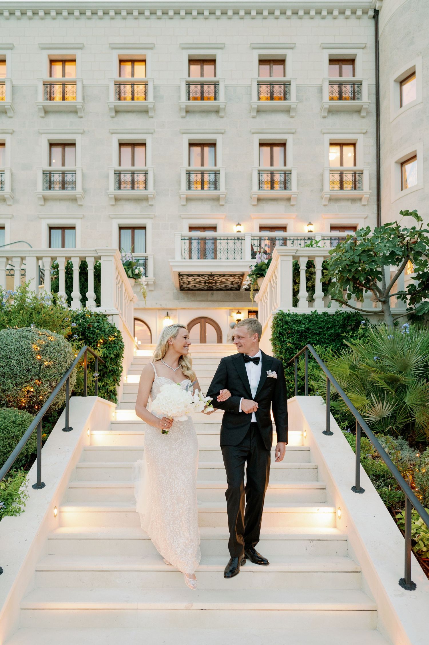 Couple descending elegant white stairs at luxury Mediterranean-style venue.