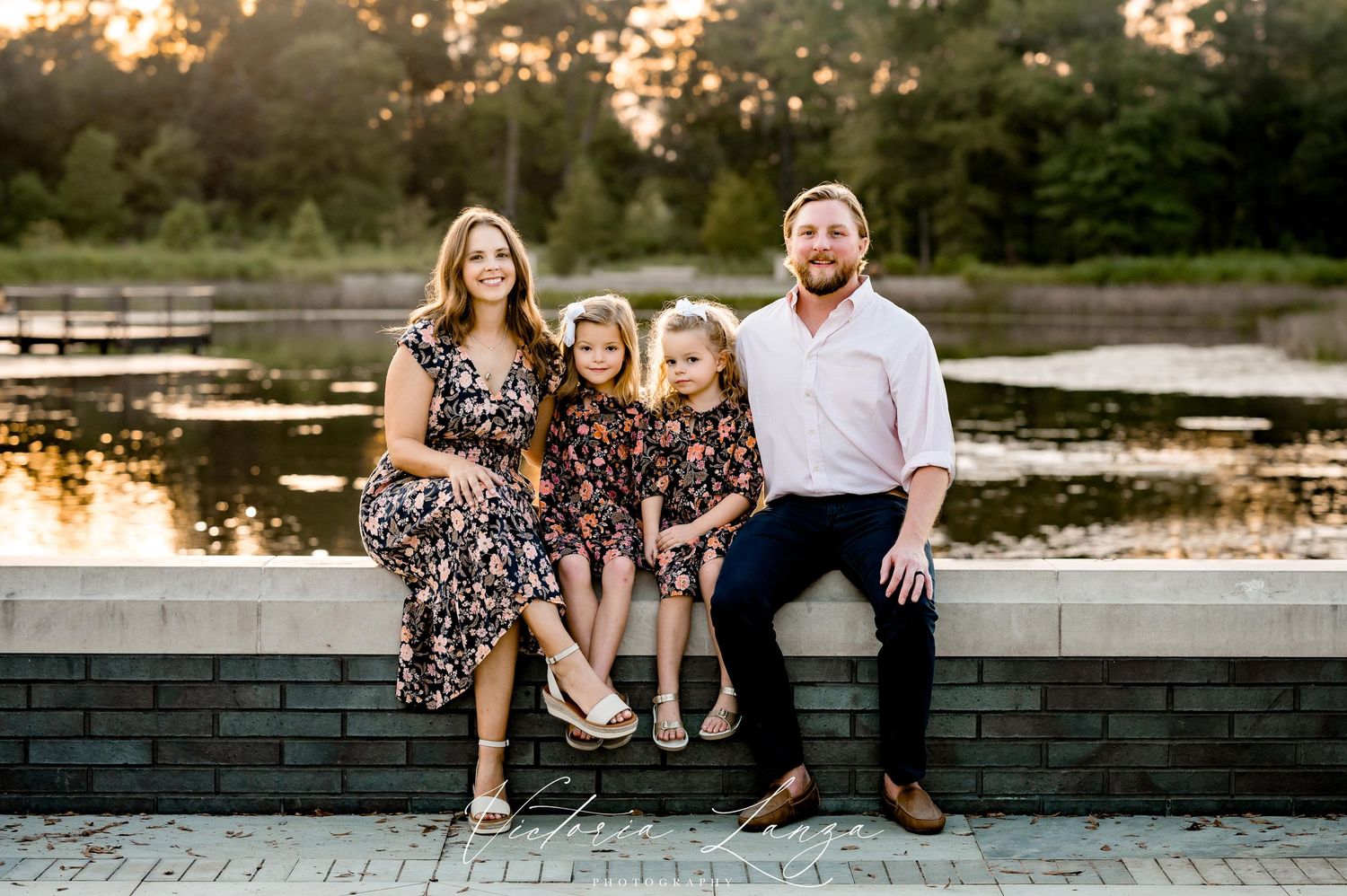 Family sitting together on stone wall by a lake during golden hour sunset.