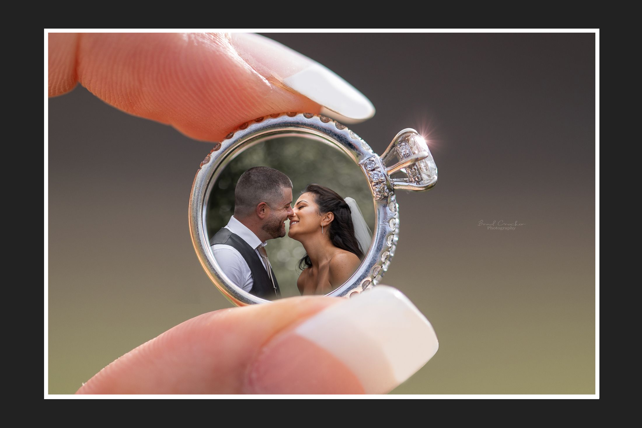 A wedding photo displayed inside a diamond engagement ring held between fingers.