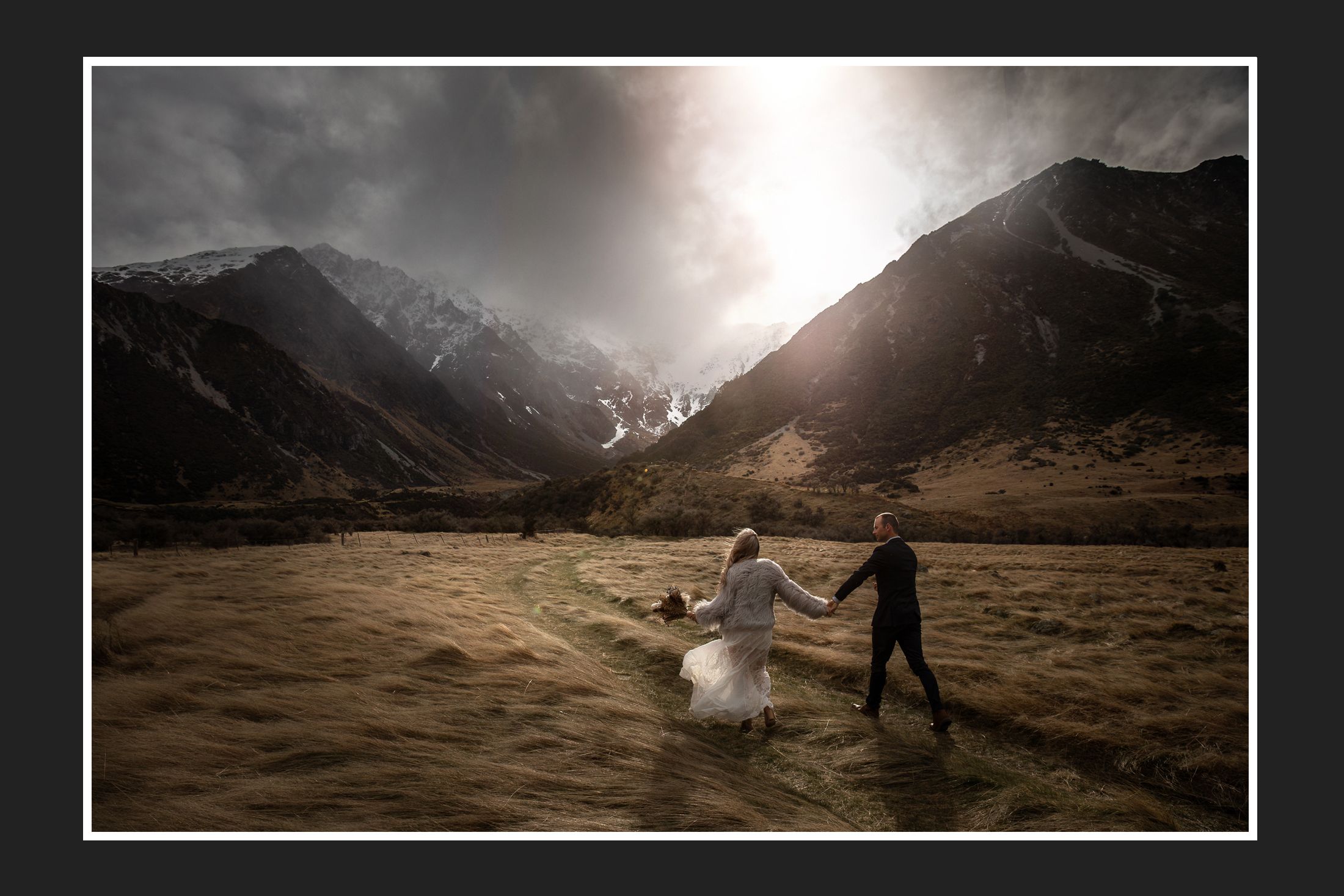 Silhouetted couple walking through a dramatic mountain valley at sunset.