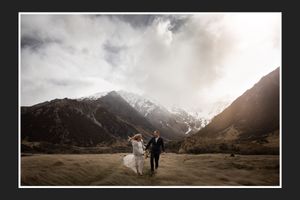 A couple walks hand in hand against a backdrop of snow-capped mountains in a valley.
