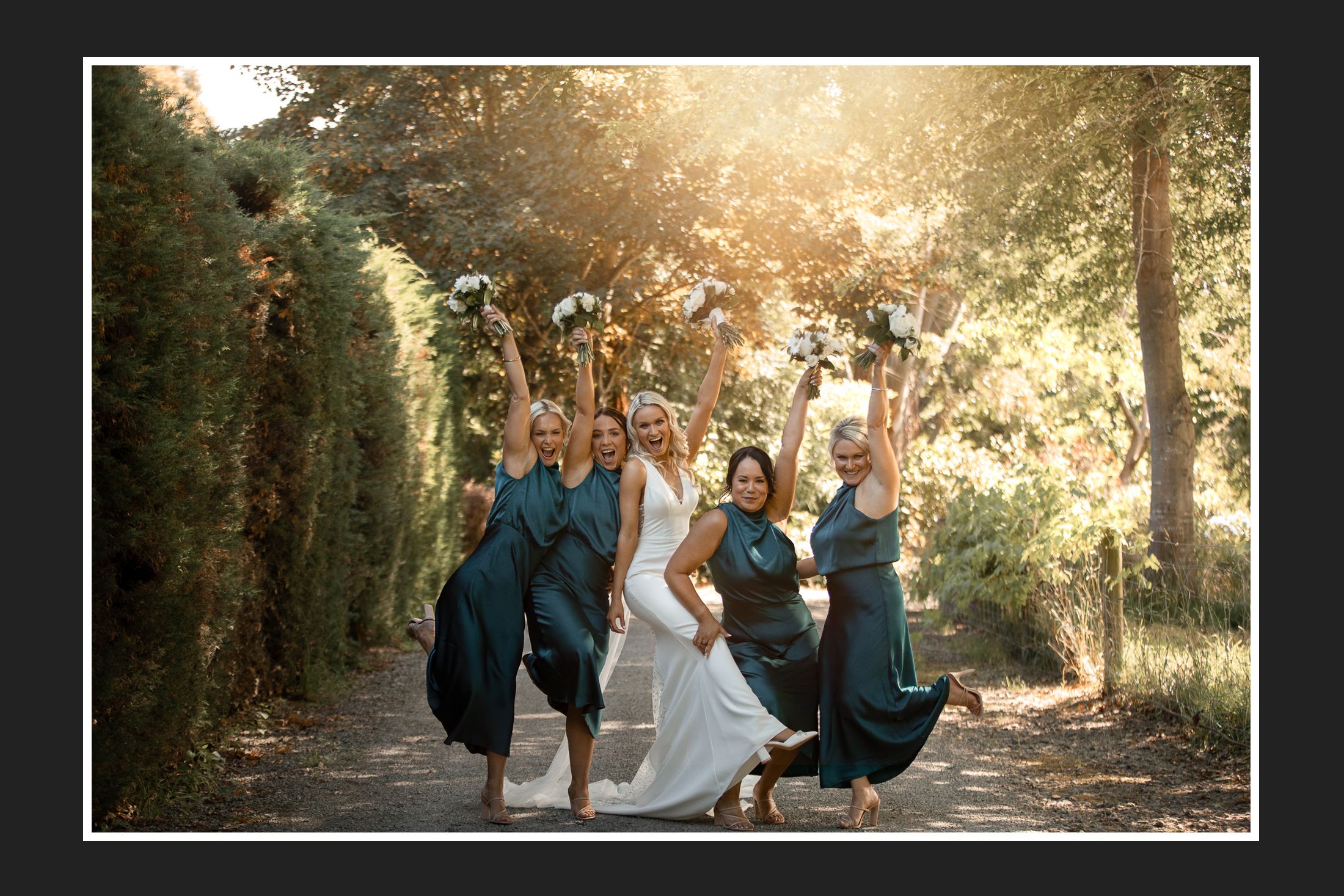 A joyful wedding party jumping in the air on a sunlit forest path.