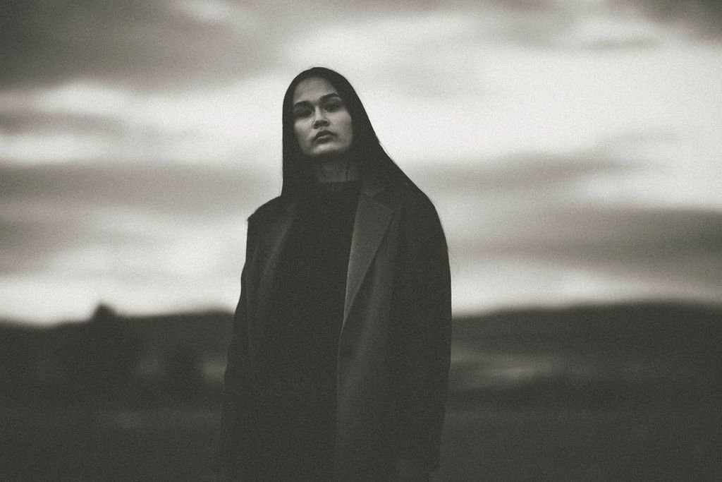 Dramatic portrait in black clothing against moody winter sky.