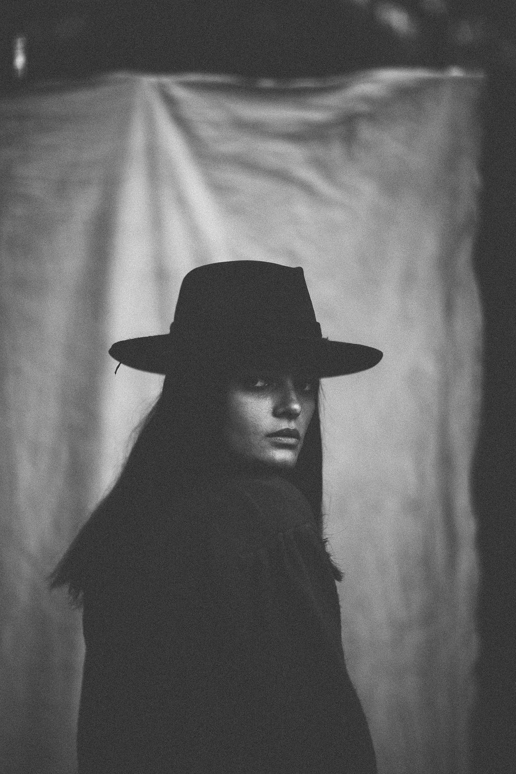 Moody black and white silhouette featuring wide-brimmed hat and long dark hair.