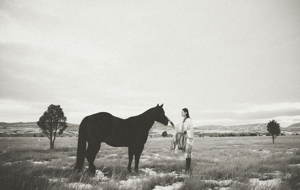Black and white landscape photograph of horse and figure in open field.