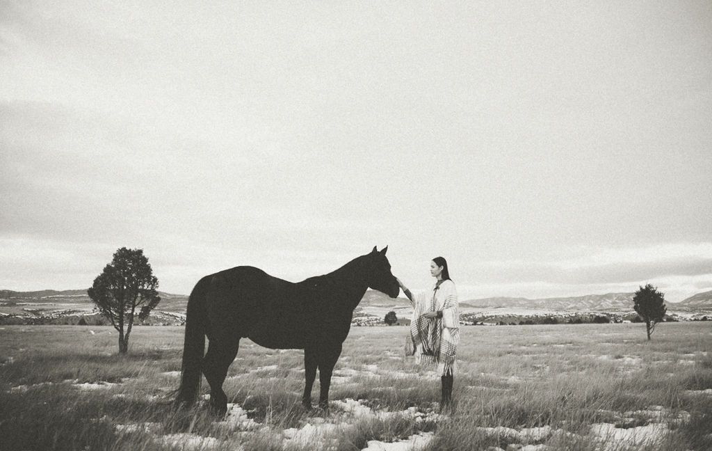 Black and white landscape photograph of horse and figure in open field.