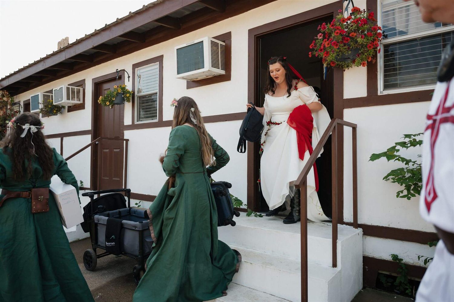 People in long green dresses gather at the entrance of a white building with brown trim.