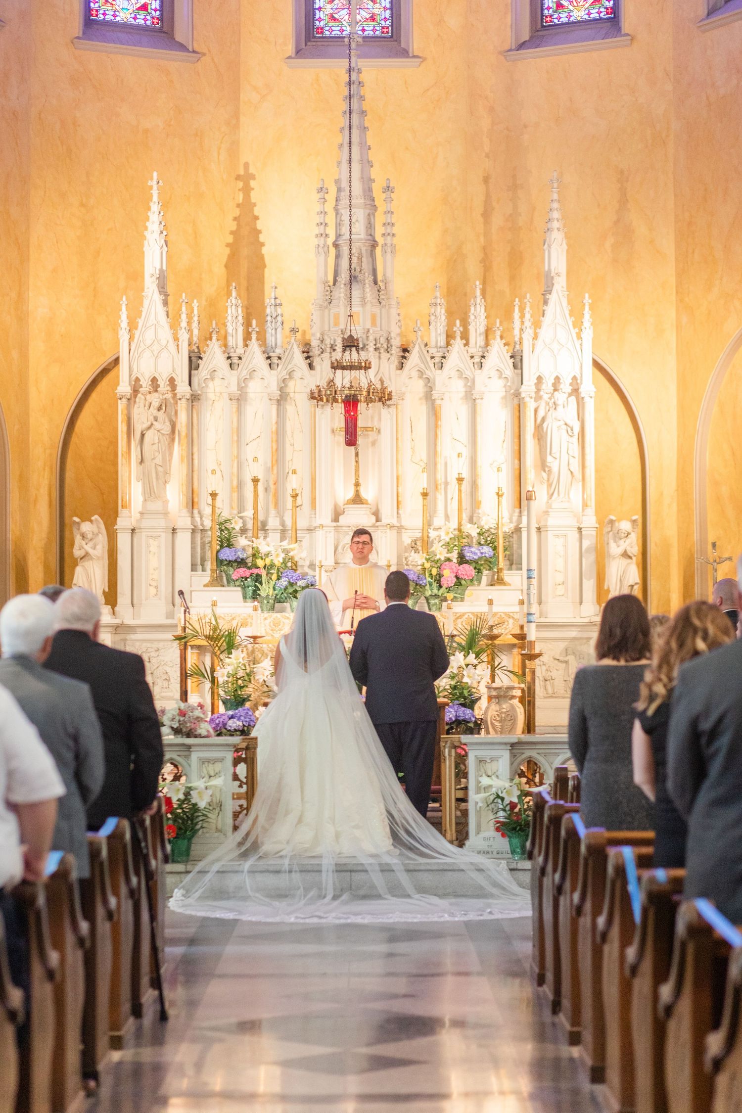 Cathedral wedding ceremony with ornate gothic altar and stained glass windows.